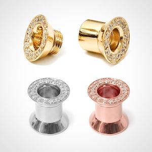 May include: Four pieces of jewelry: two gold-colored and two silver-colored. Each piece has a circular design with a ring of small, clear stones around the edge. The gold pieces have a screw-like design on one end.