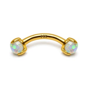 May include: A curved, gold-colored eyebrow ring with opal gemstones at each end. The opal stones have a mix of white, blue, and green colors. The ring is marked with "14K".