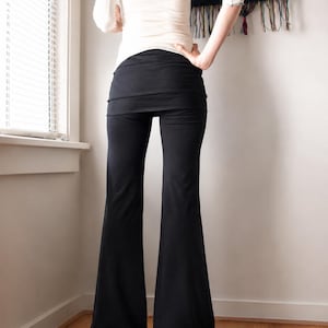 K&ouml;nnte beinhalten: Schwarze Schlaghose mit einem breiten, umklappbaren Bund. Die Hose ist an H&uuml;ften und Oberschenkeln eng anliegend und geht in eine ausgestellte Beinform &uuml;ber, die bis zum Boden reicht. Der Stoff wirkt glatt und ist in einem einheitlichen Schwarz.