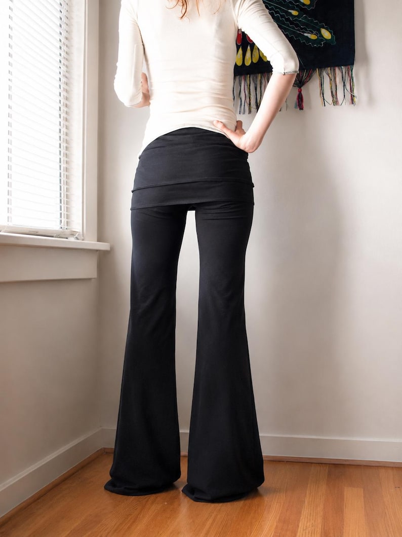 K&ouml;nnte beinhalten: Schwarze Schlaghose mit einem breiten, umklappbaren Bund. Die Hose ist an H&uuml;ften und Oberschenkeln eng anliegend und geht in eine ausgestellte Beinform &uuml;ber, die bis zum Boden reicht. Der Stoff wirkt glatt und ist in einem einheitlichen Schwarz.