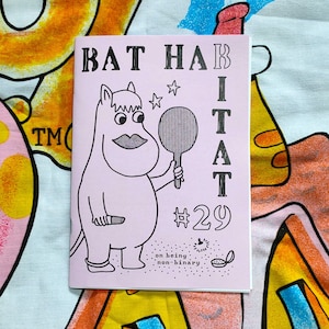 Può includere: Una copertina di rivista rosa e bianca con il titolo "BAT HABITAT #29" e il testo "on being non-binary". La copertina presenta un'illustrazione di un cartone animato di una creatura rosa che tiene uno specchio da mano.