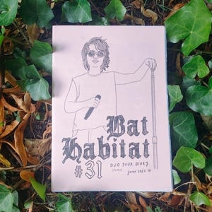 May include: A pink paper with a black and white illustration of a person holding a microphone and a cane, with the text "Bat Habitat #31". The image is surrounded by green leaves and brown foliage.