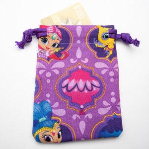 May include: Purple drawstring bag with a pattern of cartoon characters and ornate designs. The bag is made of fabric and has a purple drawstring.