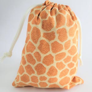 May include: A drawstring bag with a giraffe print. The bag is orange and cream-colored, with a repeating pattern of giraffe spots. It has a white drawstring closure.