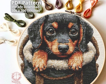 May include: A cross-stitch embroidery project in a wooden hoop featuring a black and tan puppy inside a basket. The image includes text reading PDF Pattern Instant Download 300 x 300 Stitches and Najima Cross Stitch with various colored embroidery floss.