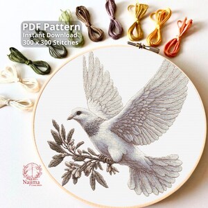 Può includere: Un modello a punto croce con una colomba bianca con le ali spiegate, che tiene un ramo d'ulivo. Il disegno è ambientato in un telaio da ricamo in legno. L'immagine include il testo "PDF Pattern Instant Download 300 x 300 Stitches". Fili colorati per ricamo sono disposti.