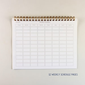 May include: A white weekly schedule notepad with a gold spiral binding. The notepad is open, displaying a grid layout for time slots and days of the week. The text "12 WEEKLY SCHEDULE PAGES" is printed at the bottom.