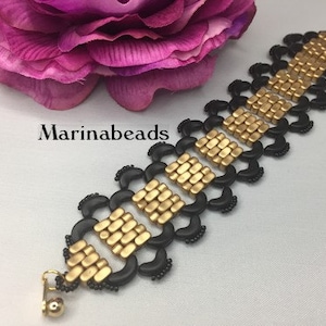 May include: A gold and black bracelet with a distinctive design. The bracelet features gold-coloured square beads and black, crescent-shaped accents. The text "Marinabeads" is visible. The bracelet is a piece of jewellery.