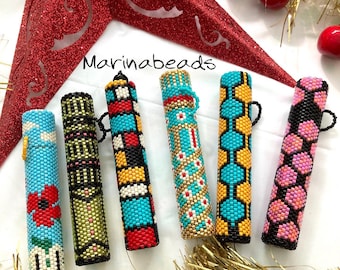 May include: Six colorful beaded pen holders with different geometric patterns. The holders are made with small beads in shades of blue, yellow, red, black, white, and pink. The text "Marinabeads" is visible in the image.