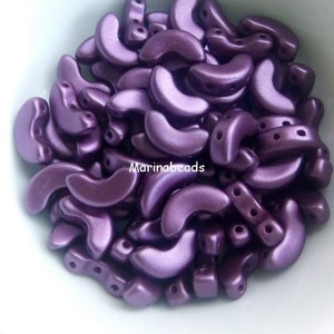May include: A bowl filled with purple crescent-shaped beads. The beads have a metallic sheen and are approximately 10mm in size.