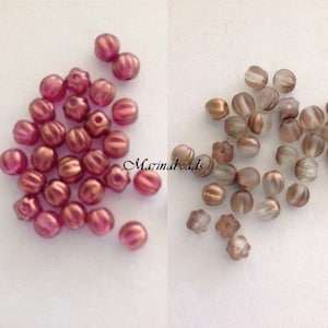 May include: Two groups of glass beads. One group is pink with a metallic sheen, the other is clear with a metallic sheen. Both groups have a ribbed texture.