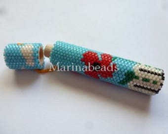 May include: A turquoise beaded tube with a wooden stopper, featuring a red flower and green leaves design. The tube is open, revealing the wooden interior. The design includes white and black accents. The text "Marinabeads" is visible.