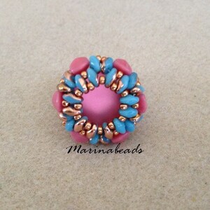 May include: A pink and blue beaded ring with a copper wire design. The ring is made of small, round beads and has a circular shape.
