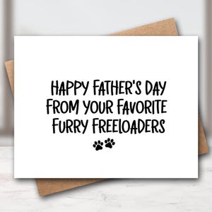 May include: A white Father's Day card with the message "Happy Father's Day From Your Favorite Furry Freeloaders" in black text. Two black paw prints are below the text. The card is on a brown envelope.
