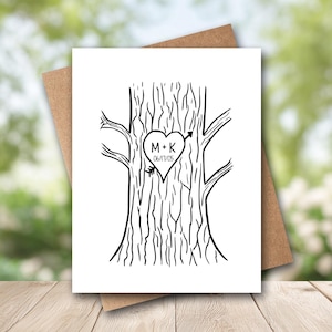 May include: A white greeting card featuring a black line drawing of a tree trunk with a heart carved into the bark. Inside the heart, the text M + K is written above the date 06/17/05, with an arrow piercing through the heart shape.