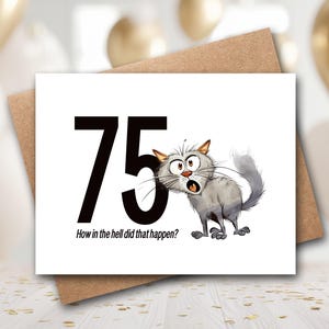 May include: A white greeting card featuring the large black number 75 and a cartoon illustration of a wide-eyed, surprised gray cat. Below the number, the text reads, How in the hell did that happen? The card is placed on a brown paper envelope.