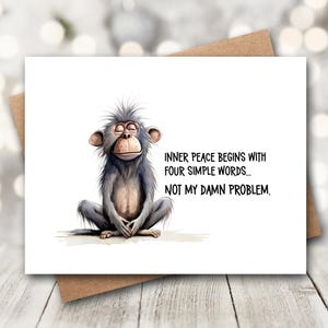 May include: A greeting card featuring a cartoon monkey in a meditative pose. The monkey is gray with a light brown face and is sitting cross-legged. The card reads, "Inner peace begins with four simple words... NOT MY DAMN PROBLEM."