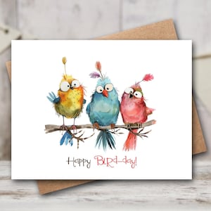 May include: A greeting card featuring three whimsical birds perched on a branch. The birds are in shades of yellow, blue, and pink, with large eyes and feathery details. The text "Happy Bird-day!" is written below the birds.