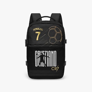Könnte beinhalten: Schwarzer Rucksack mit goldenem Text und Grafiken. Der obere Bereich zeigt "RONALDO" über der Nummer "7" und eine Fußballgrafik. Der untere Bereich hat "CRISTIANO" und "CR7" in Weiß. Mit zwei Schultergurten und einem oberen Griff.
