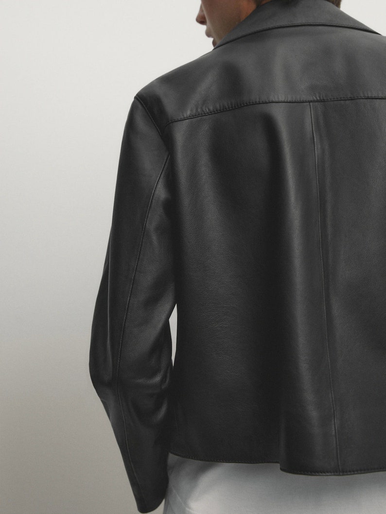 May include: A black leather jacket with a collared neckline and long sleeves. The jacket has a simple design and a slightly cropped hem.