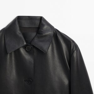 May include: A black leather jacket with a button-up front and two pockets. The jacket has a collar and is made of a soft, supple leather.