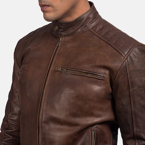 Könnte beinhalten: Eine braune Lederjacke mit Reißverschluss und mehreren Taschen. Die Jacke hat einen Stehkragen und ein gestepptes Design an den Schultern.