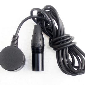 Puede incluir: Un micrófono negro con un micrófono redondo negro con cable conectado a él. El micrófono tiene un cable negro con un enchufe negro en el extremo.