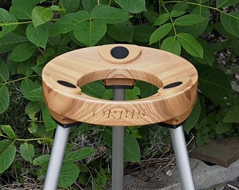 May include: A wooden tripod table with a circular top and three legs. The top has a central opening and three smaller circular indentations. The word "ORBIS" is engraved on the front. The legs are silver-colored.