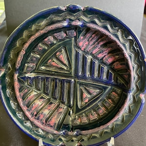 May include: A round ceramic dish with a blue and green glaze. The dish has a raised design of geometric shapes in pink and blue.
