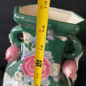 May include: A green ceramic vase with floral designs and pink accents. The vase has two handles and measures 15 inches tall.