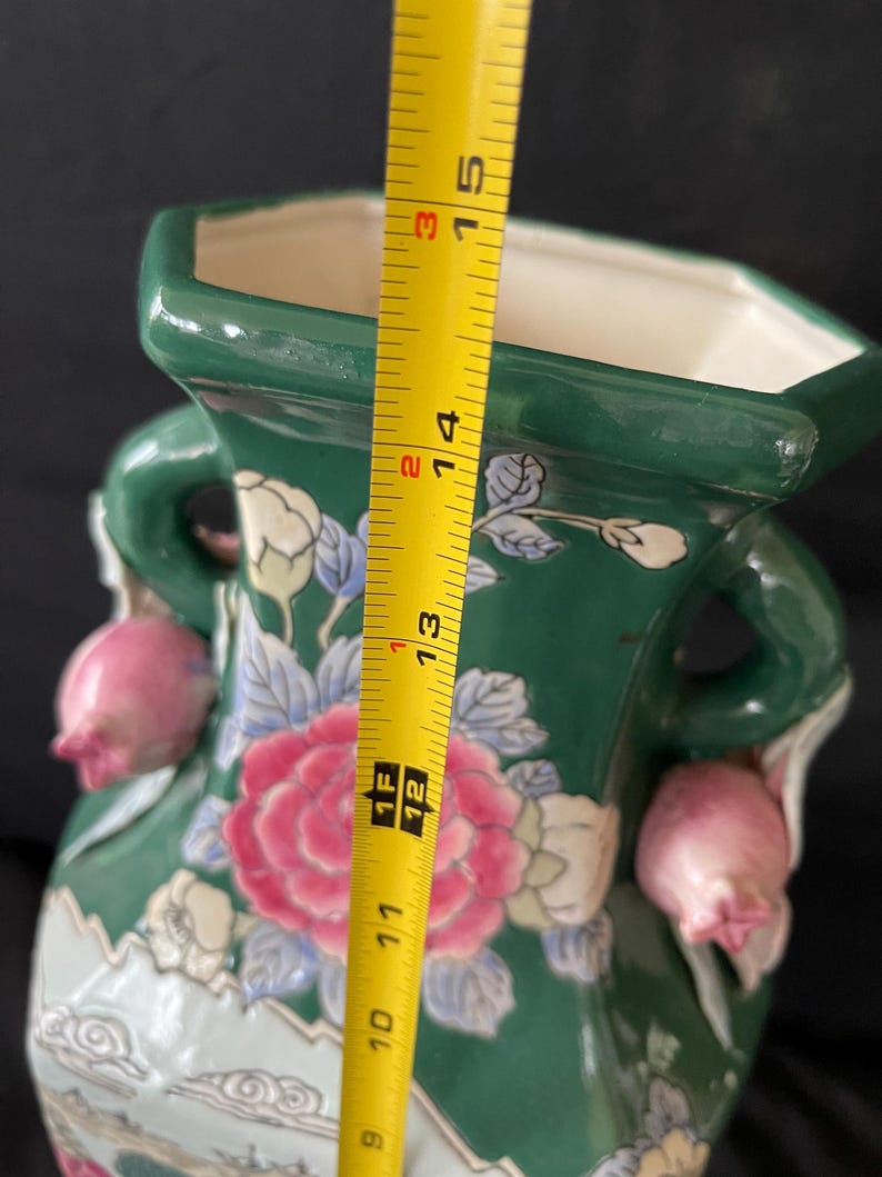 May include: A green ceramic vase with floral designs and pink accents. The vase has two handles and measures 15 inches tall.