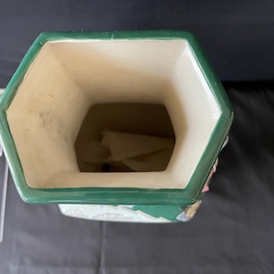 May include: A green and white ceramic vase with a hexagonal opening. The vase has a floral design with pink, green, and white accents.