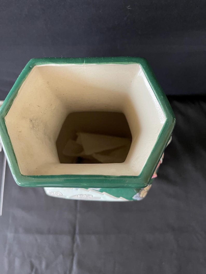 May include: A green and white ceramic vase with a hexagonal opening. The vase has a floral design with pink, green, and white accents.