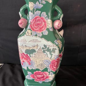 May include: A green ceramic vase with floral and landscape designs. The vase has two handles with pink fruit accents.
