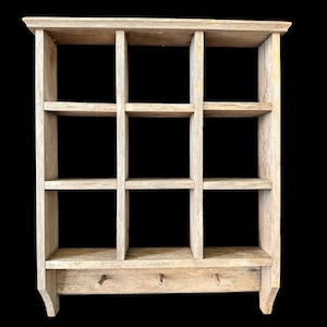 Könnte beinhalten: Ein helles Wandregal aus Holz mit neun Fächern und drei Haken darunter. Das Regal hat eine rechteckige Form mit einer leicht überhängenden Oberseite und ist aus hellfarbigem Holz gefertigt.