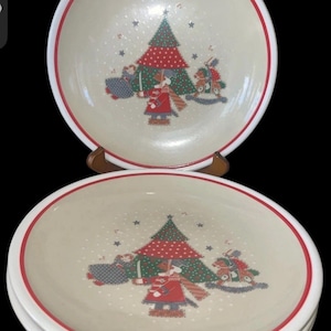 Puede incluir: Juego de platos con temática navideña. Cada plato presenta un centro color crema con un borde rojo y un diseño festivo de un árbol de Navidad, un soldado y un caballito balancín. Los platos están apilados, mostrando el diseño.