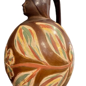 Puede incluir: Jarra de cerámica marrón con asa y diseño de rostro en el pico. El cuerpo de la jarra está decorado con coloridos diseños de hojas en tonos rojos, amarillos y verdes. La jarra tiene forma redondeada.