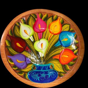 Könnte beinhalten: Handbemalte Holz-Dekorplatte mit floralem Design. Sie zeigt Calla-Lilien in Rot, Pink, Gelb, Orange, Blau, Grün und Lila, angeordnet in einer blauen Vase. Der Durchmesser der Platte beträgt etwa 30 cm.