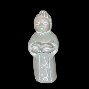 May include: A ceramic figurine of a person singing, holding a book. The figure is dressed in a long robe with a series of white circles down the front. The figurine is painted in shades of gray and white, with a black background.