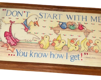 May include: Framed artwork featuring a cartoon goose and ducklings. The goose wears a pink and blue outfit, with the text "DON'T START WITH ME... You know how I get!" in blue. The frame is made of wood.