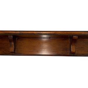 May include: A wooden shelf with a dark brown finish. The shelf has a rounded front edge and is supported by two decorative brackets. The shelf is designed to be mounted on a wall and is suitable for displaying items.