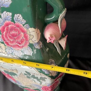 May include: A green ceramic vase with a floral design and a handle shaped like a pomegranate. The vase is approximately 8 inches tall.