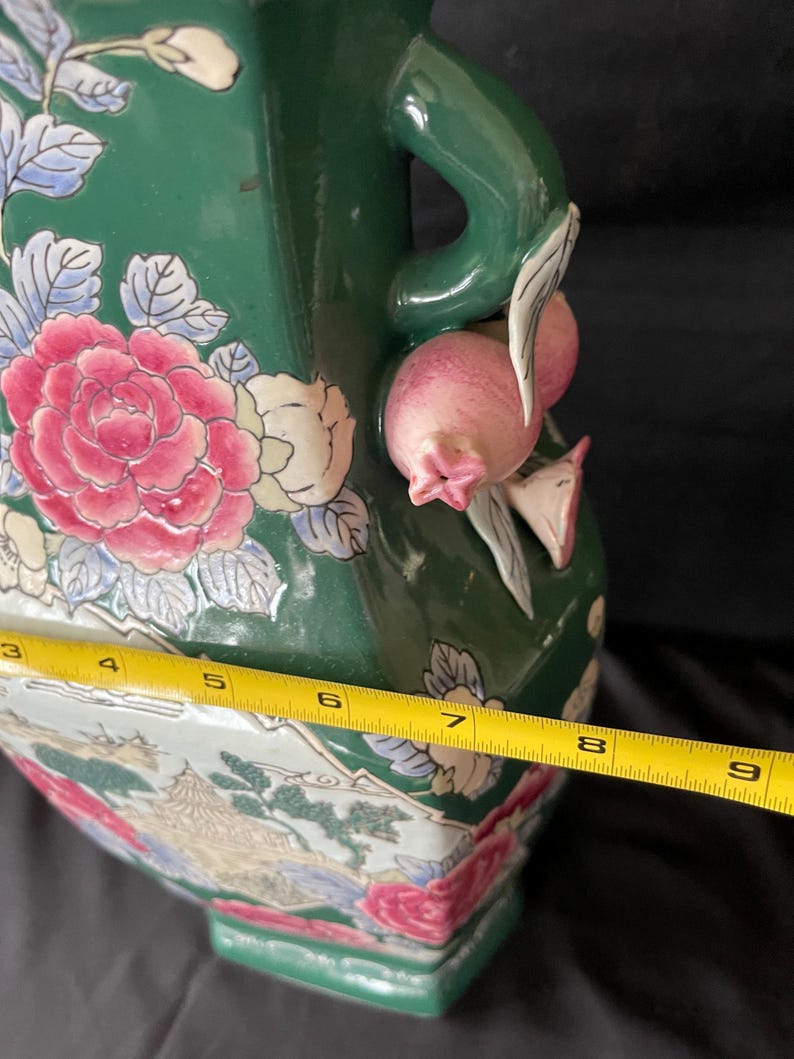 May include: A green ceramic vase with a floral design and a handle shaped like a pomegranate. The vase is approximately 8 inches tall.