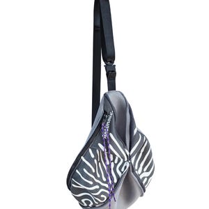 May include: A gray and white patterned sling bag with a black adjustable strap. The bag has a zipper closure and a purple drawstring. The bag has the text "Air.made." printed on the side.