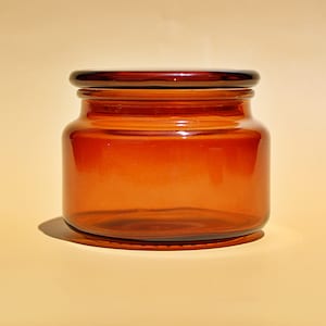 Peut inclure: Un pot en verre ambré transparent avec un couvercle. Le pot est vide et a un fond arrondi.
