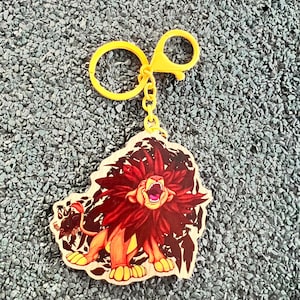 May include: A yellow keychain with a lion design. The lion has a red mane and is roaring with its mouth open. The keychain has a yellow ring and clasp.