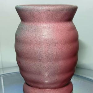 May include: A pink ceramic vase with a textured, rippled surface. The vase has a rounded body and a flared lip.