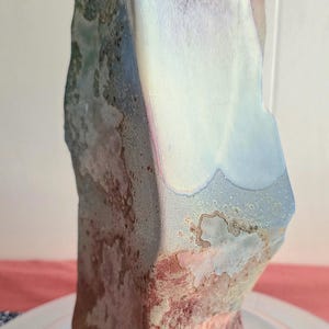 May include: A vertical ceramic sculpture with a textured, multi-coloured glaze. The surface features a blend of muted blue, soft pink, and earthy brown tones with a matte finish. The form is irregular and upright, resembling a natural stone formation.