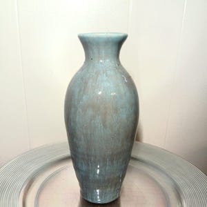 May include: A tall, ceramic vase with a flared top and a rounded body. The vase has a mottled blue-green glaze with a glossy finish. It is displayed on a silver-colored, textured tray. The vase is a decorative item.