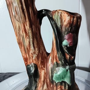May include: A ceramic vase shaped like a tree trunk with brown, green, and red glaze. The vase has two openings for flowers.